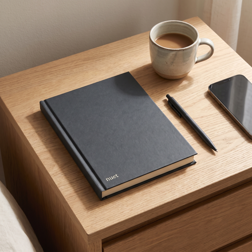 Nuet journal på natbord med kaffe, pen og telefon vendt nedad